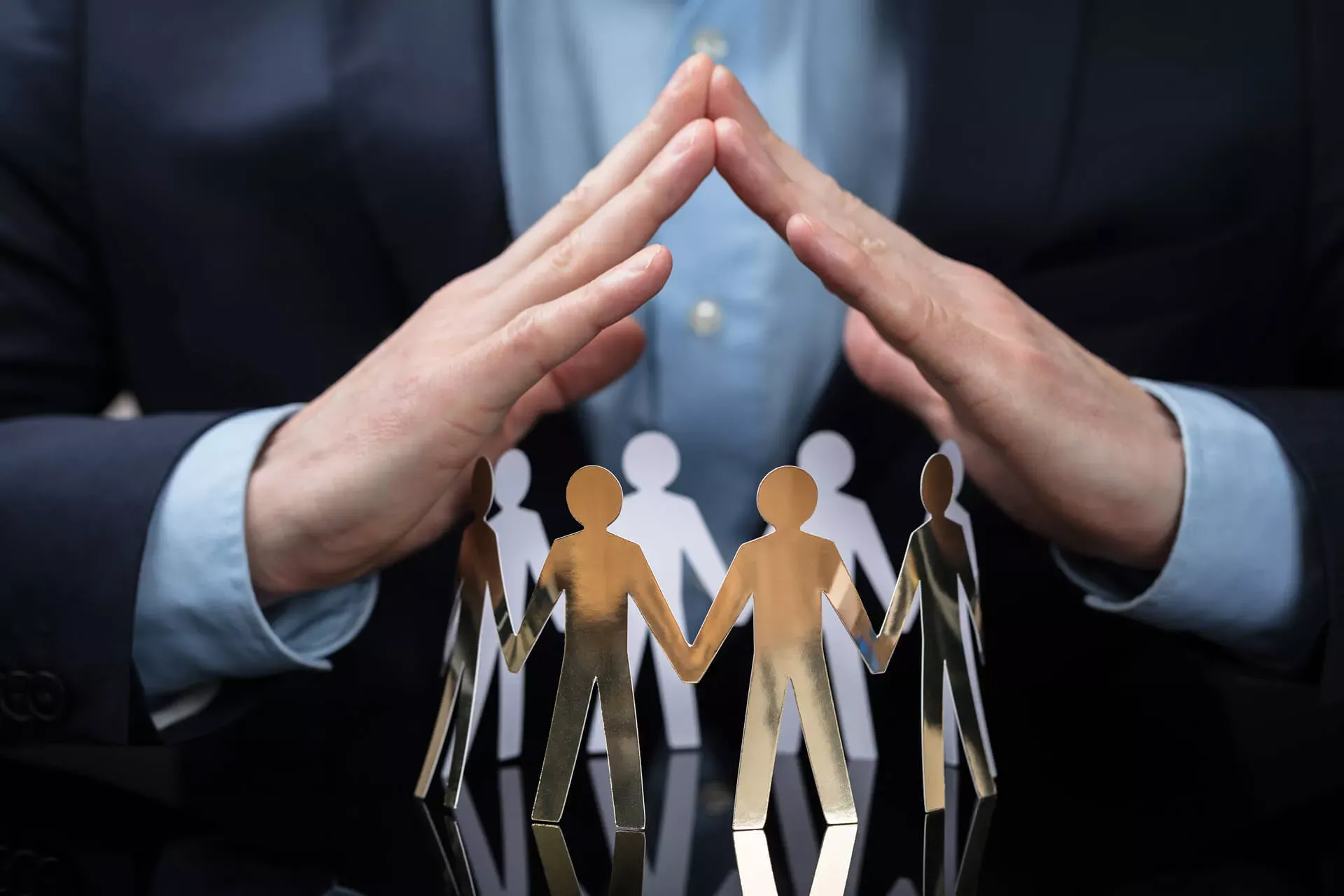 Betriebsrat: Hände eines Mannes bilden ein Dach über einem Kreis von Papierfiguren, die sich an den Händen halten. Betriebsrat: Hände eines Mannes bilden ein Dach über einem Kreis von Papierfiguren, die sich an den Händen halten.