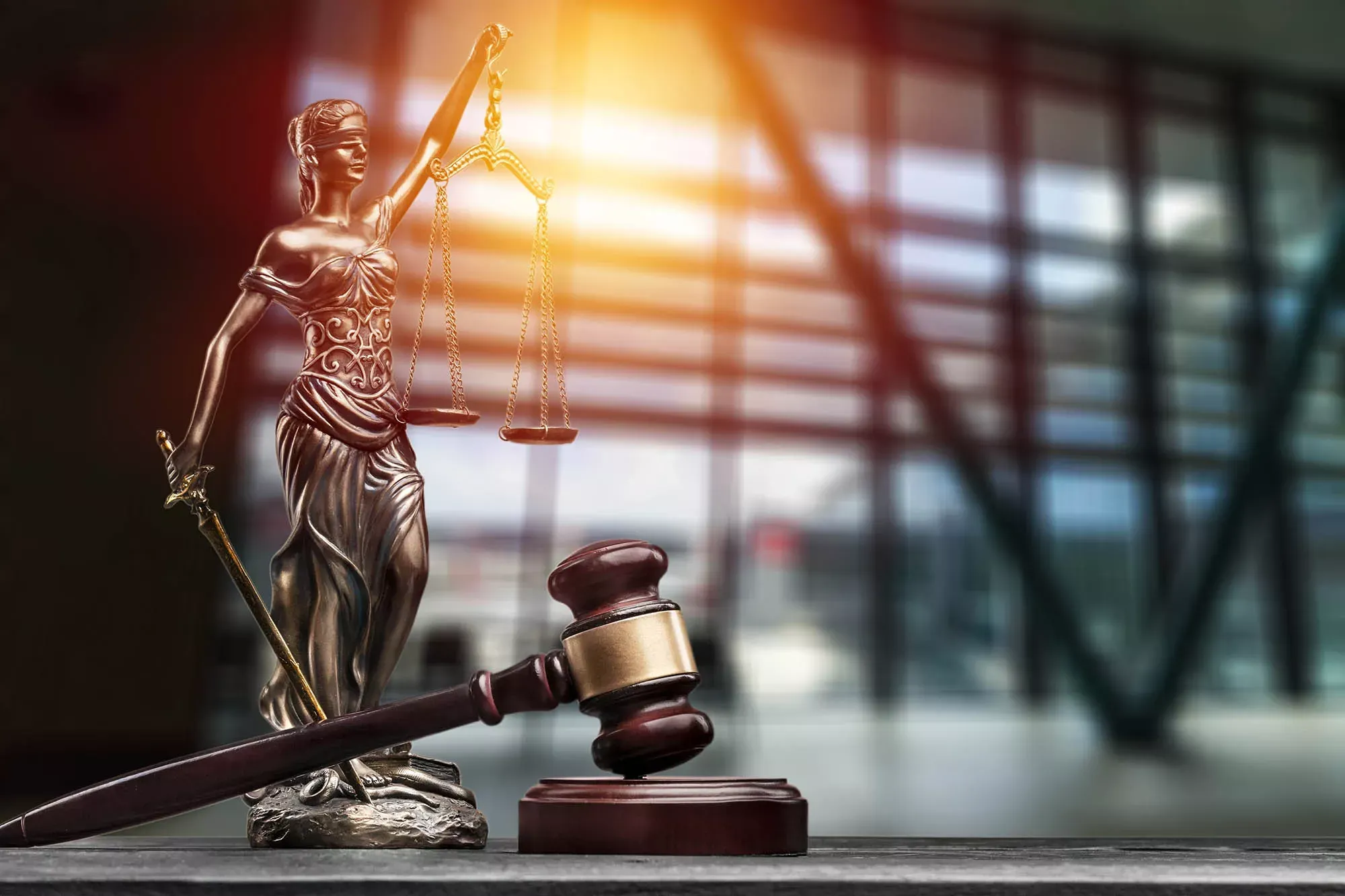 Bronze-Statuette der Justizia mit Richterhammer vor einem Fenster. Bronze-Statuette der Justizia mit Richterhammer vor einem Fenster.