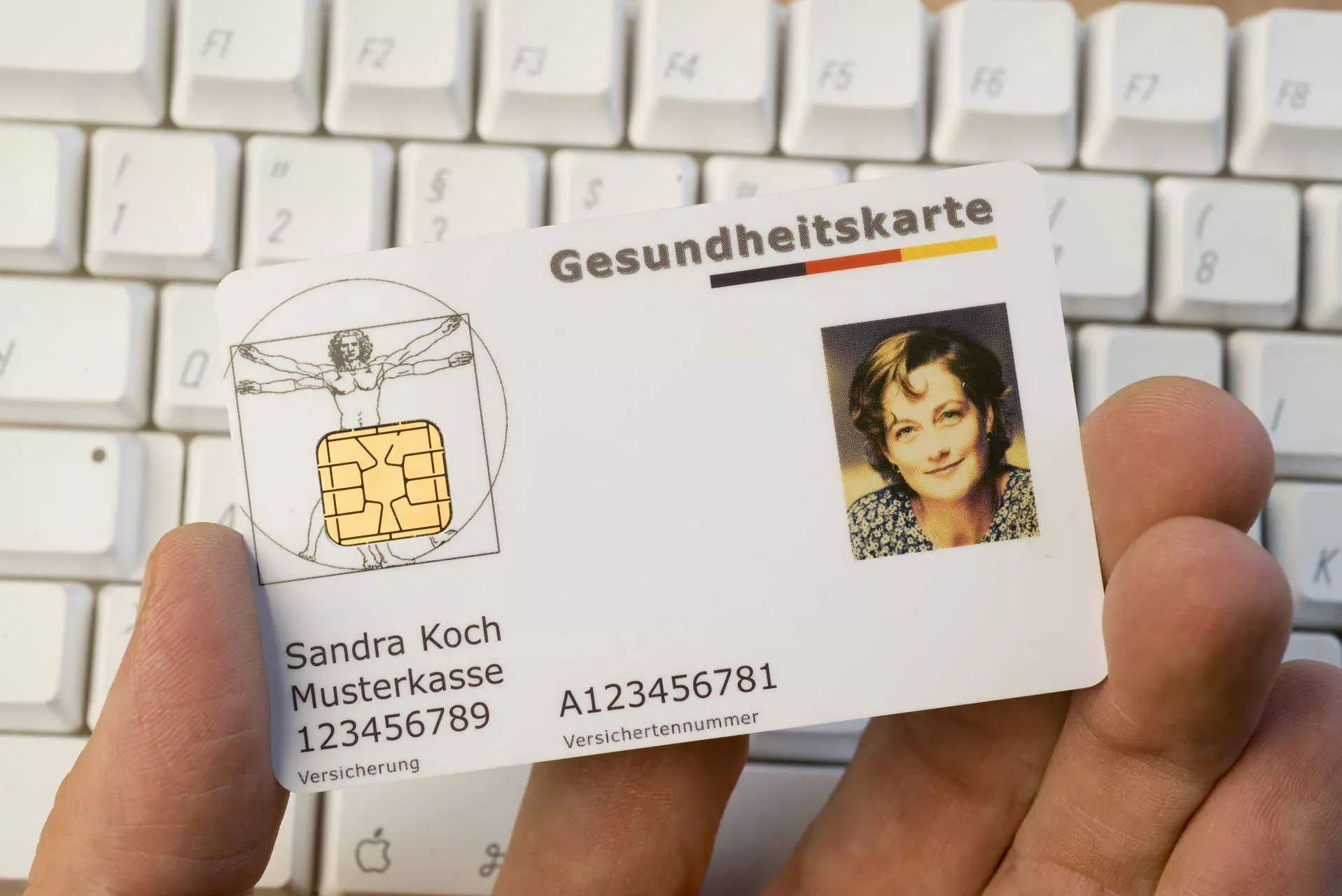 Hand hält eine Gesundheitskarte über einer Computertastatur. Bild: IMAGO / imagebroker / imago stock&people