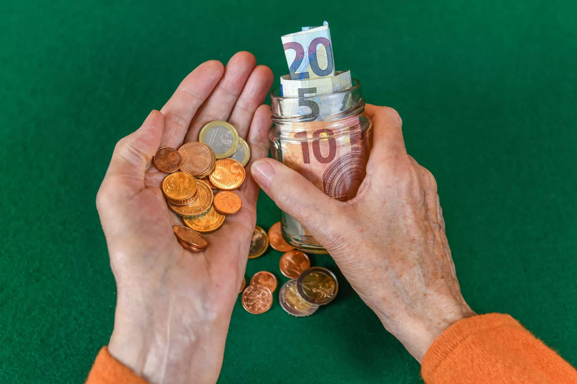 Hände einer Seniorin halten Glas mit Geldscheinen und Münzen. Bild: IMAGO / Joko