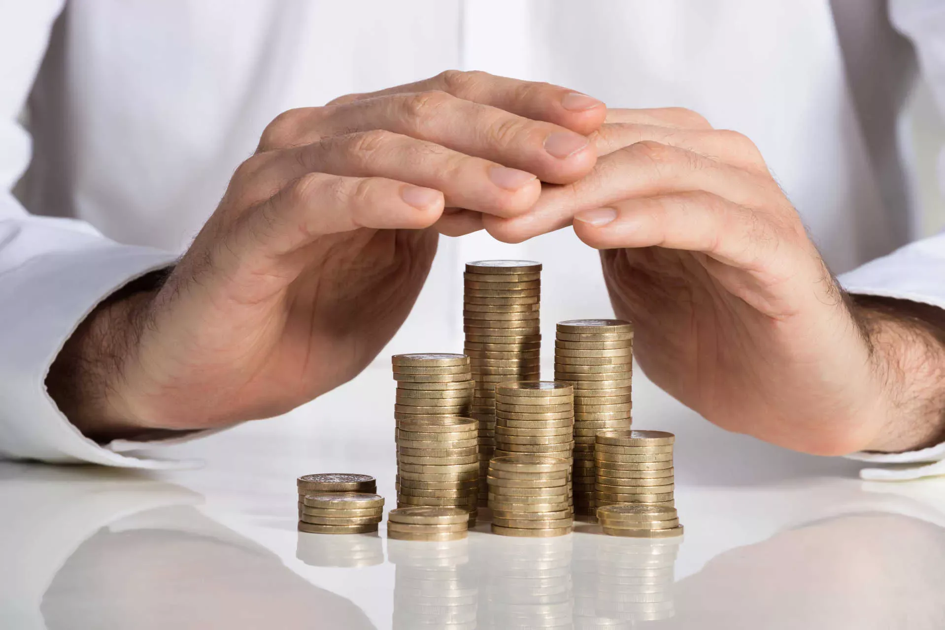 Hände legen sich schützend über das Vermögen in Form von Euro-Münzenstapel. Hände legen sich schützend über das Vermögen in Form von Euro-Münzenstapel.