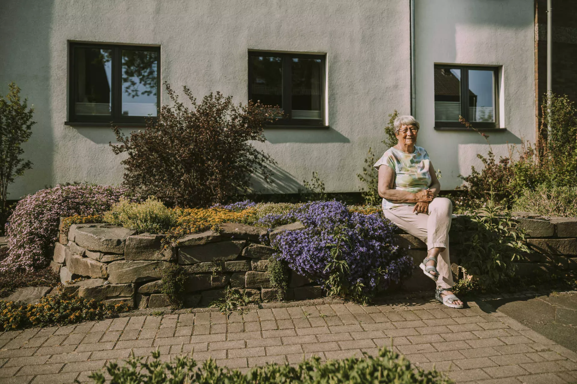 Seniorin sitzt vor ihrem Haus in der Sonne. Bild: IMAGO / Westend61 / Mareen Fischinger