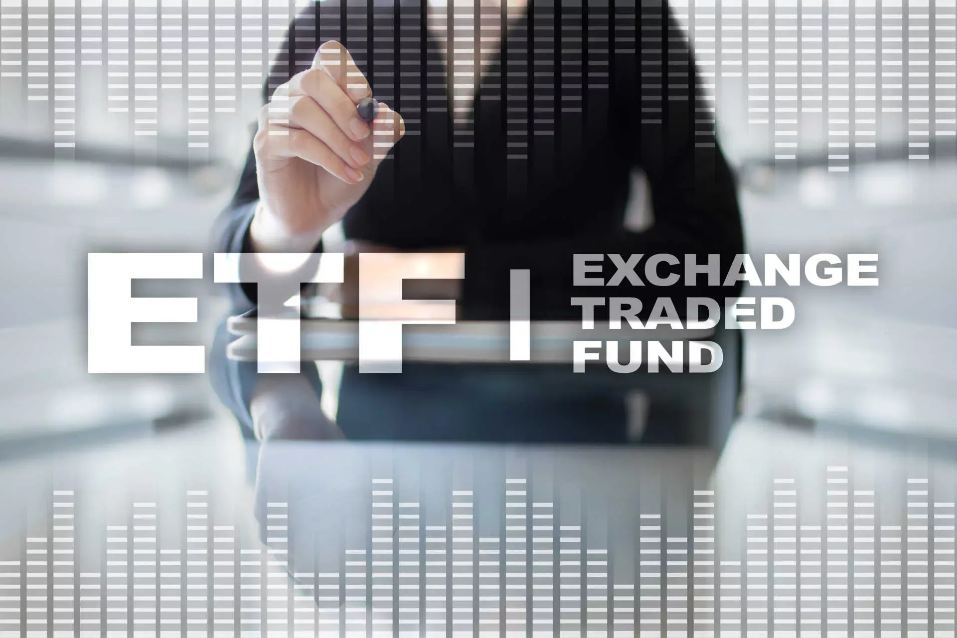 Buchstaben ETF Exchange Traded Fund in weiß auf transparenter Oberfläche, im Hintergrund zeigt Frau mit Stift darauf. Bild: IMAGO / agefotostock / Wrightstudio Buchstaben ETF Exchange Traded Fund in weiß auf transparenter Oberfläche, im Hintergrund zeigt Frau mit Stift darauf. Bild: IMAGO / agefotostock / Wrightstudio