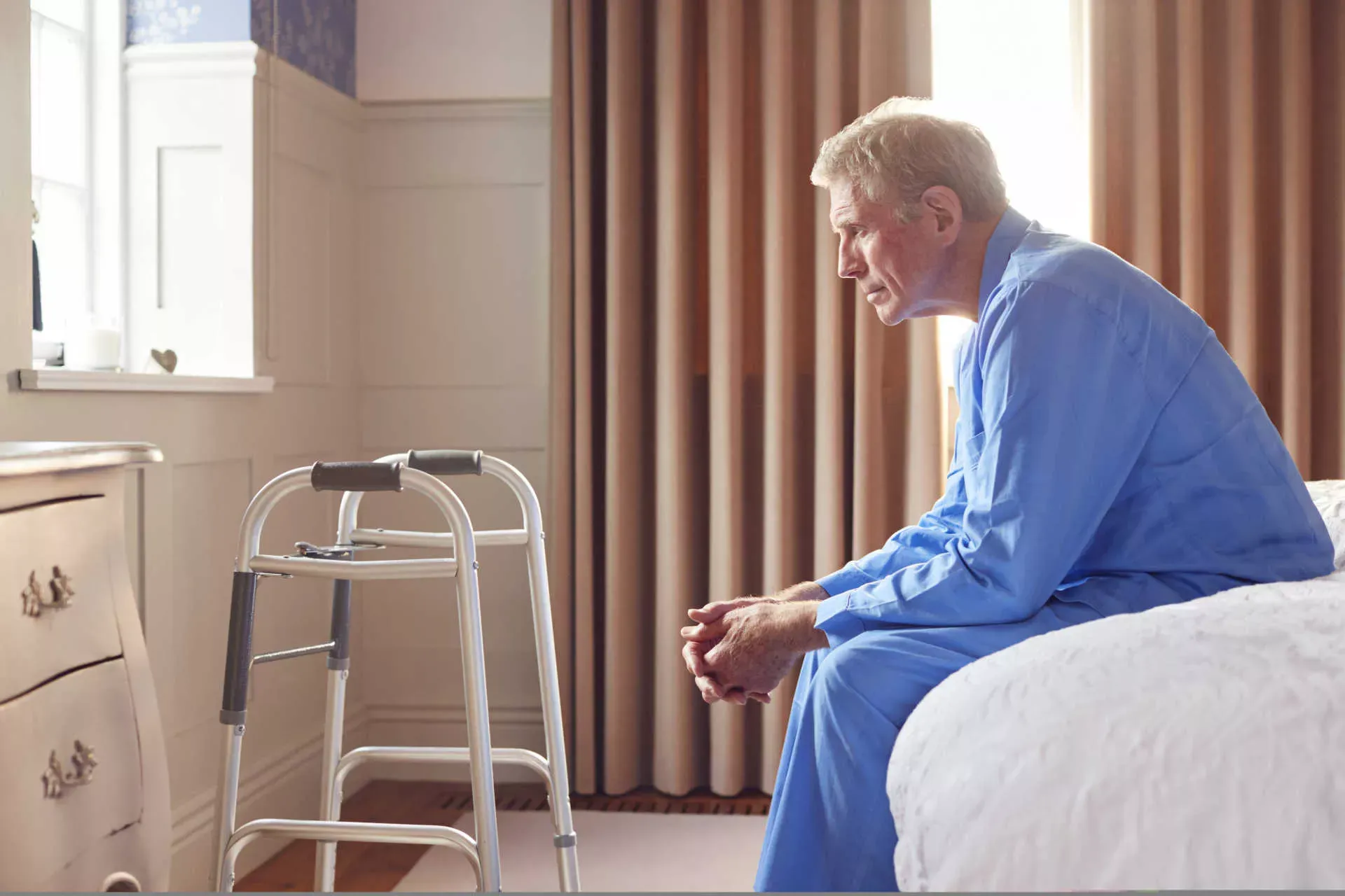 Deprimierter Senior sitzt auf dem Bettrand, vor sich eine Gehhilfe. Bild: IMAGO / Shotshop / Monkey Business 2