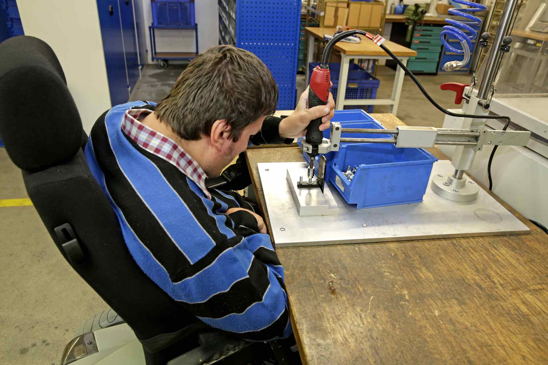 Beschreibung: Geistig und körperlich behinderter Mann bei der Arbeit an einer Werkbank Geistig und körperlich behinderter Mann bei der Arbeit an einer Werkbank