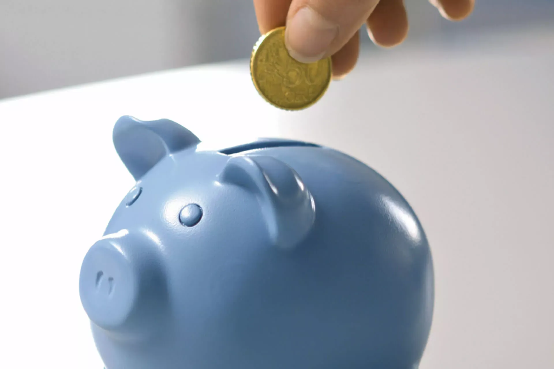 Frauenhand steckt eine 50-Cent-Münze in ein blaues Sparschwein.