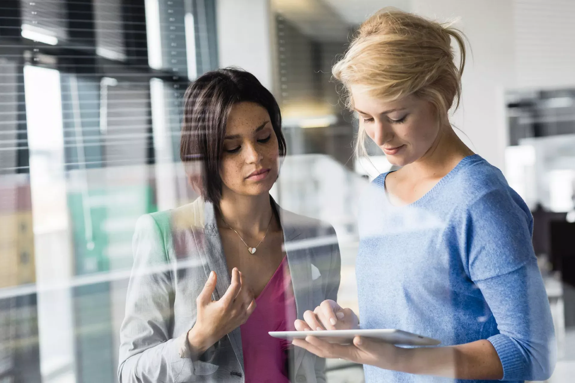 Zwei junge Frauen stehen im Büro und schauen zusammen auf ein Tablet. Zwei junge Frauen stehen im Büro und schauen zusammen auf ein Tablet.