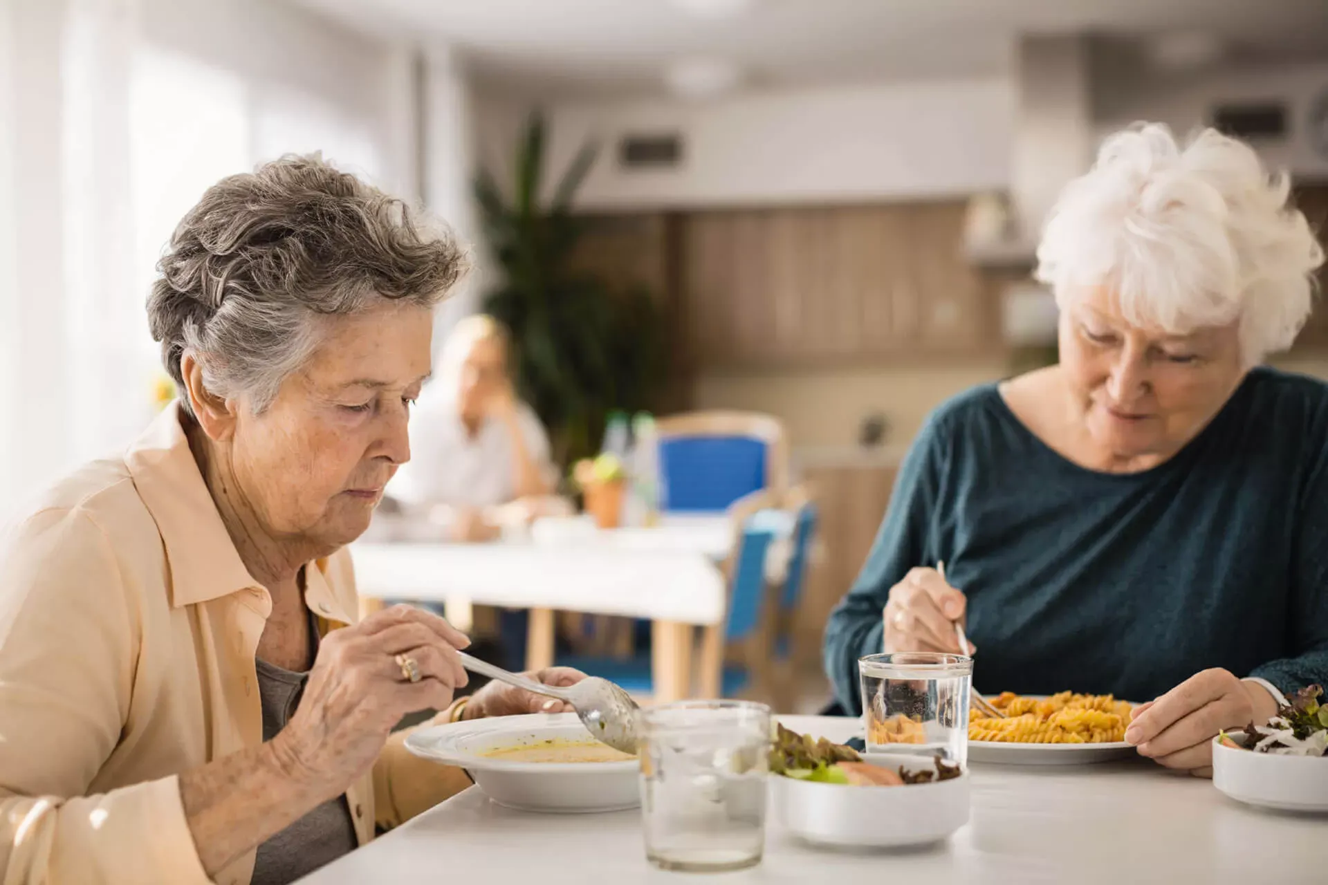 Zwei ältere Frauen sitzen an einem Tisch in einem Speisesaal und essen.
