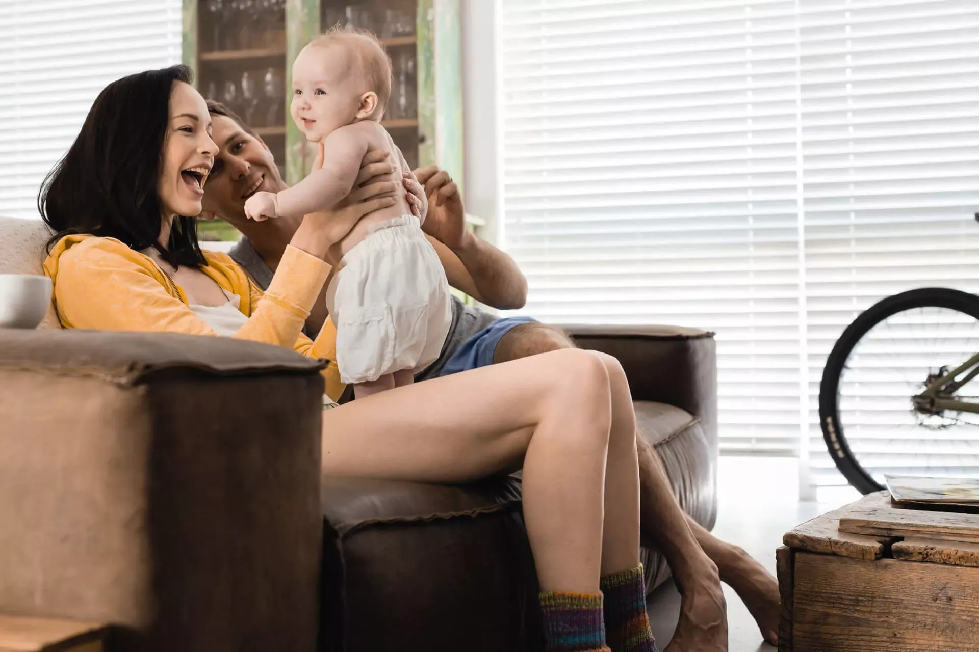 Junges Elternpaar sitzt mit Baby auf dem Sofa.