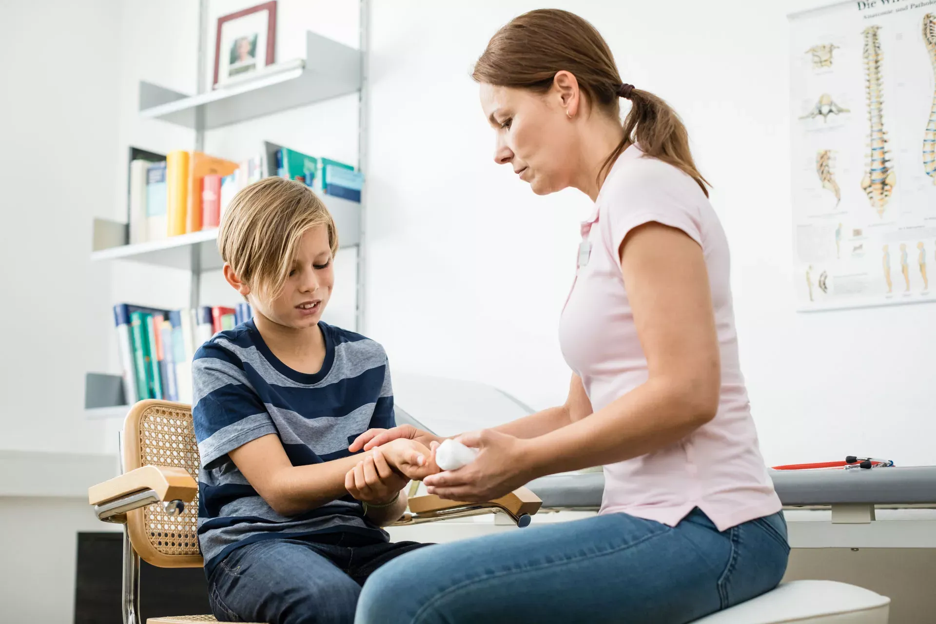Eine Kinderärztin behandelt die Handgelenkverletzung eines Jungen von ca. 10-12 Jahren Eine Kinderärztin behandelt die Handgelenkverletzung eines Jungen von ca. 10-12 Jahren