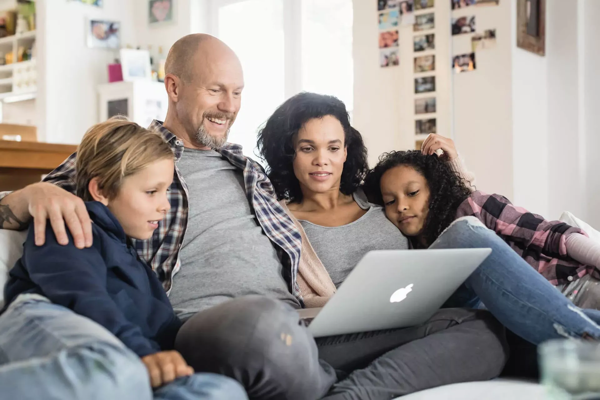 Beschreibung: Familie mit zwei Kindern sitzt auf dem Sofa und schaut auf ein Notebook. Familie mit zwei Kindern sitzt auf dem Sofa und schaut auf ein Notebook.